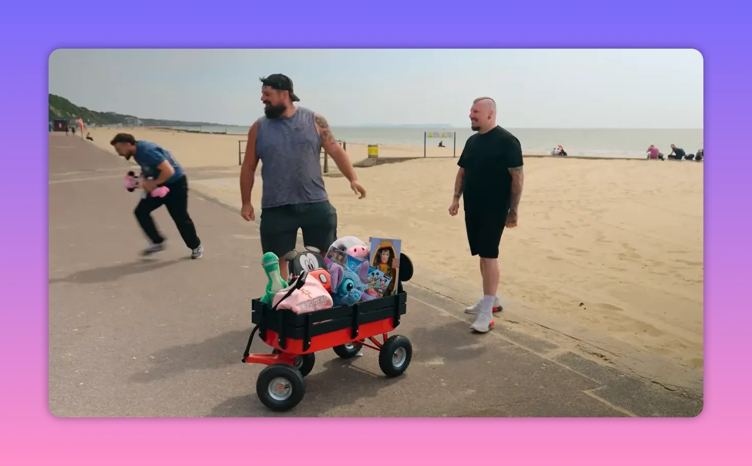 Wagon of Disney plush prizes on a beach promenade with two contestants nearby.
