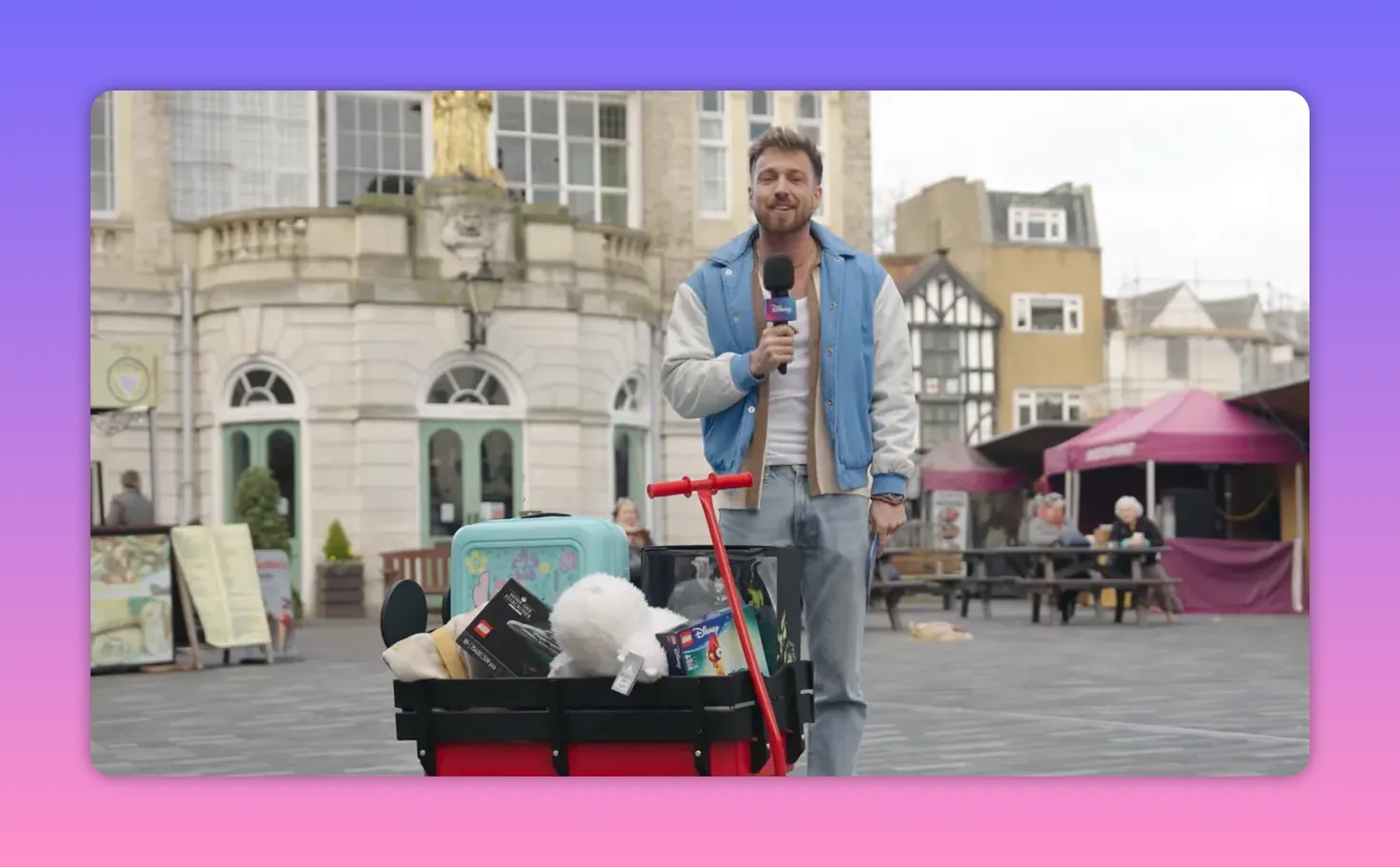 Host standing beside a red wagon filled with Disney prizes and holding a microphone.