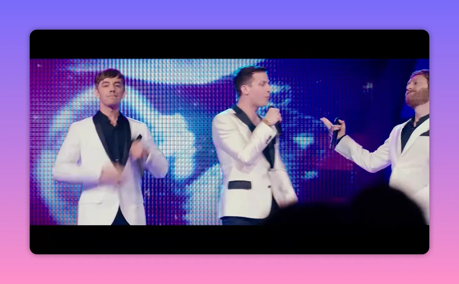 Three male performers in white jackets singing and interacting on stage with an LED backdrop