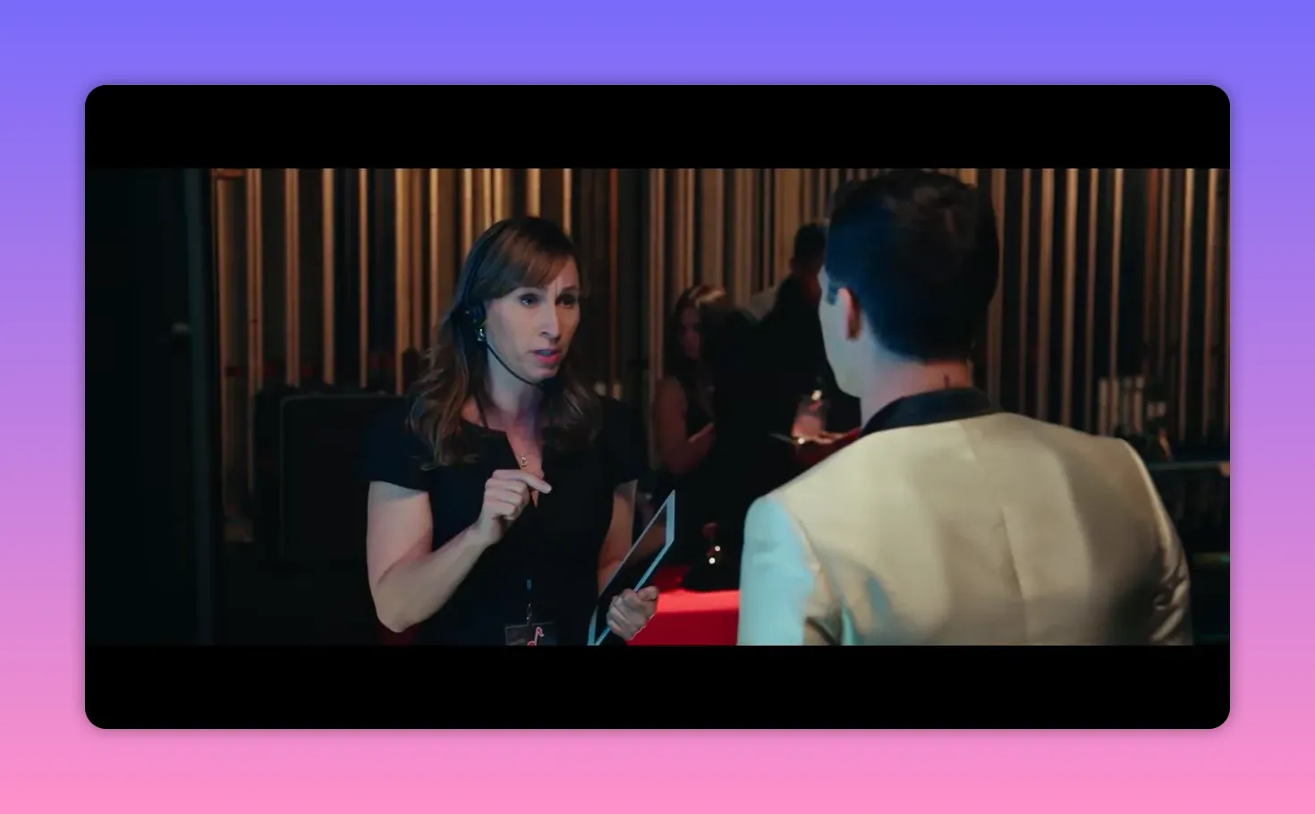 Female stage manager with headset pointing and speaking to a performer in a gold jacket backstage
