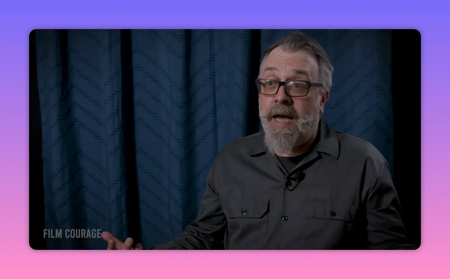 Mid-shot of a writer/teacher speaking with visible hand gesture, blue curtain background, FILM COURAGE watermark