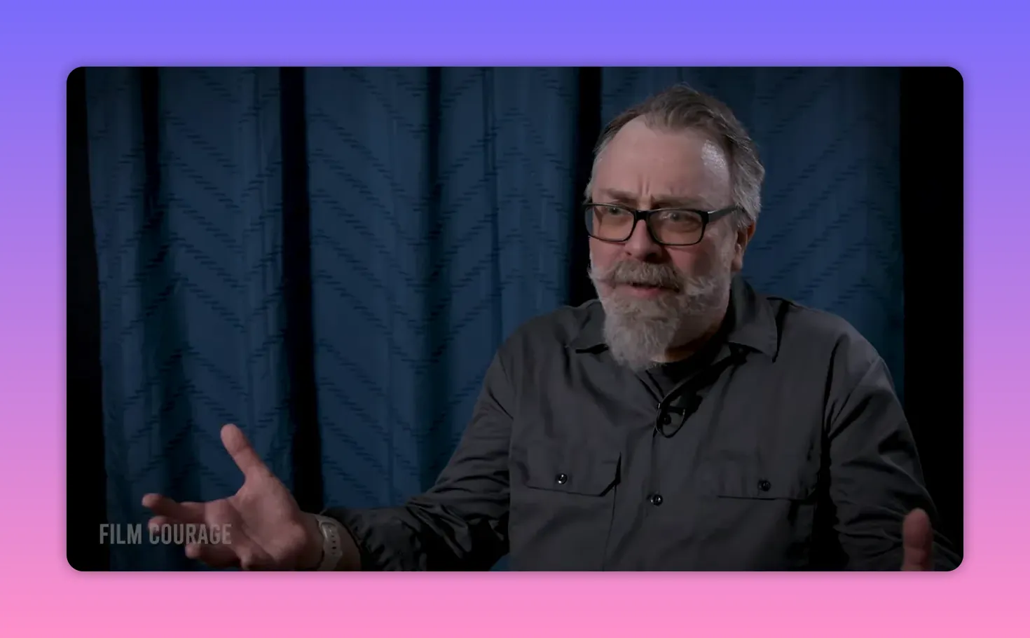 Interview subject with open hands and a calm, encouraging expression against a blue curtain backdrop