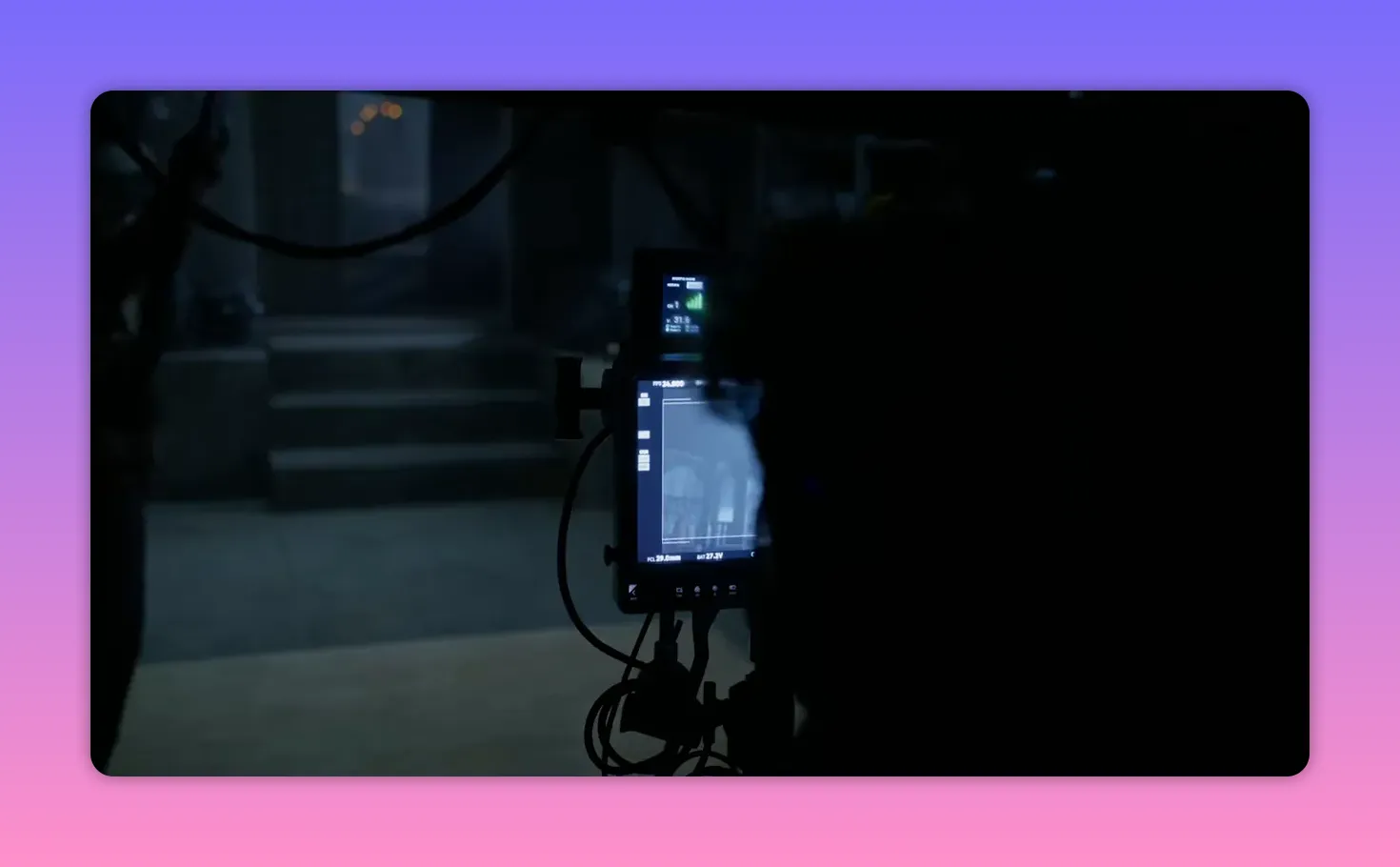 Camera monitor and rig on set showing a playback frame, with cables and shadowed crew.