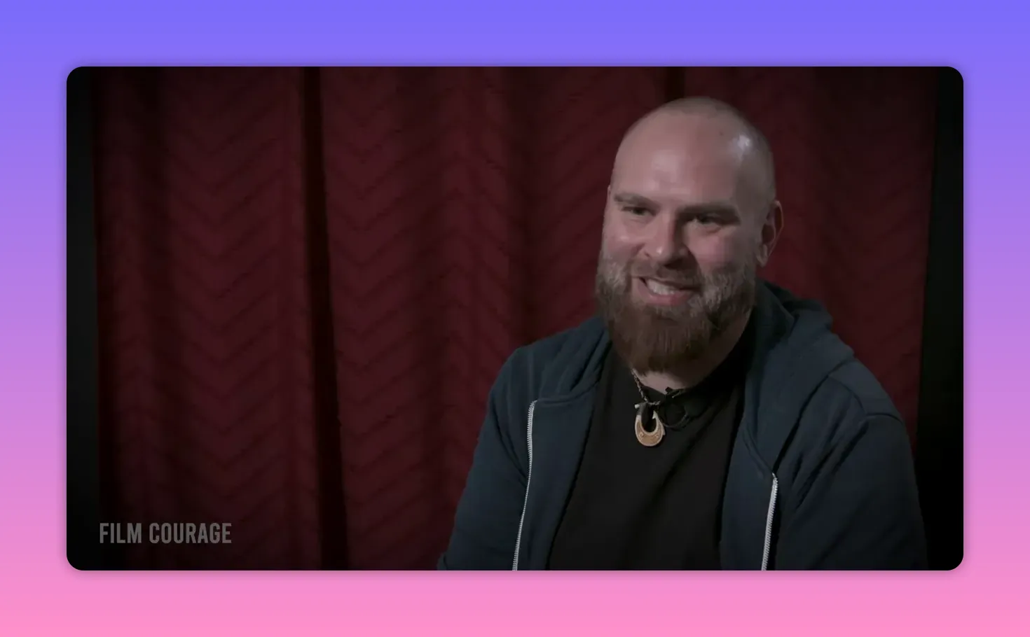 Interview subject smiling and engaged in conversation, framed against a red curtain.