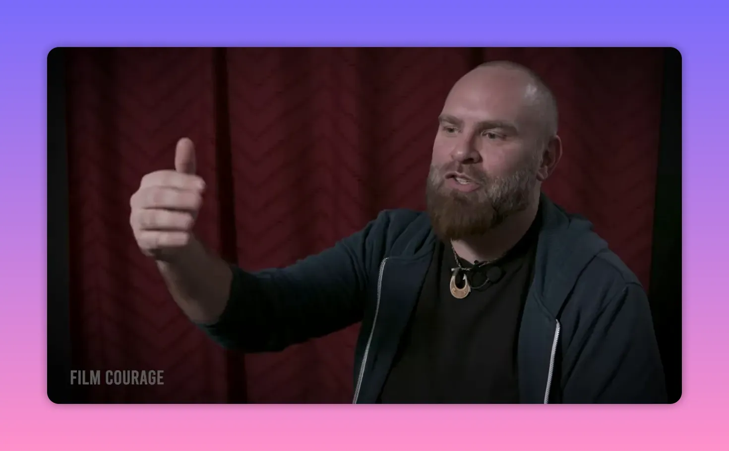 Interview subject making an open hand gesture while explaining story tools, red curtain backdrop