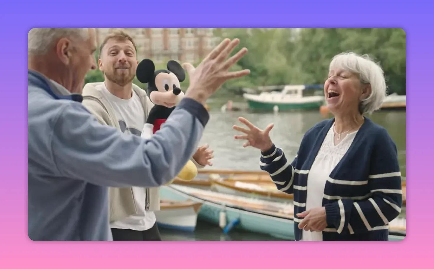 Two contestants and the host reacting with outstretched hands and laughter beside the river and a prize wagon