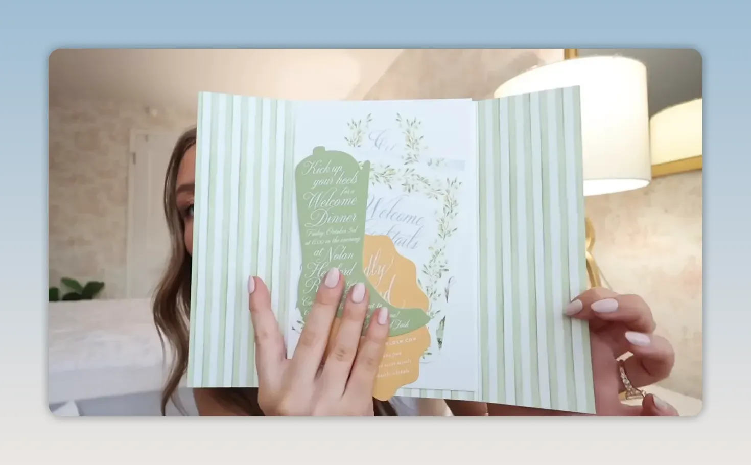 Hands holding a wedding invitation suite with green striped paper and illustrated inserts