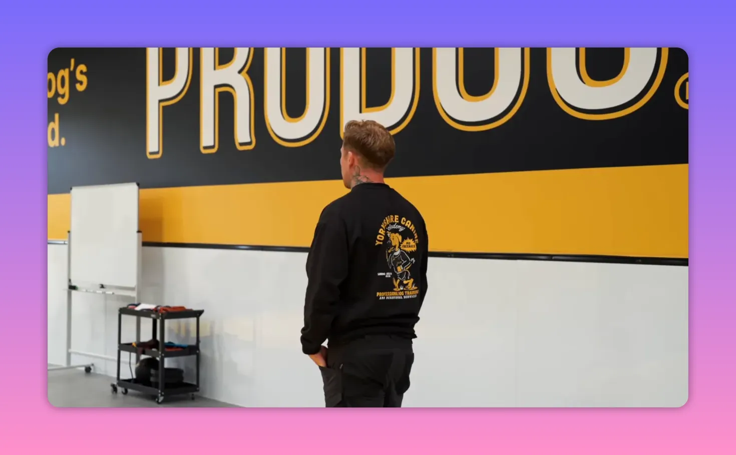 Trainer standing and looking toward the training area under a large PRODOG logo on the wall in an indoor dog training facility.