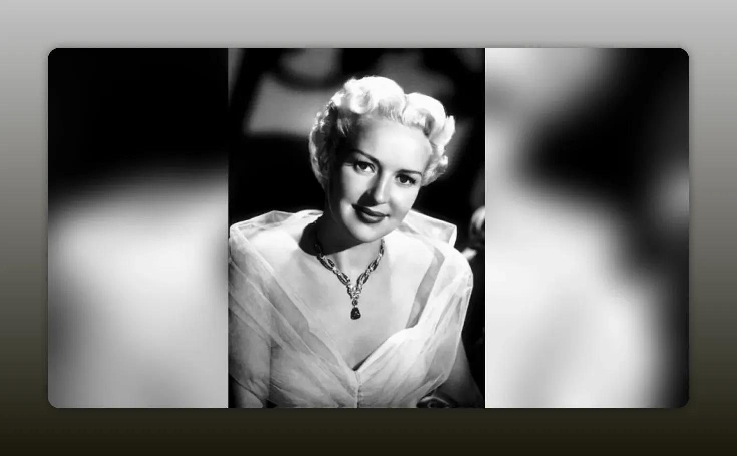High-contrast black-and-white close-up portrait of Betty Grable in a sheer dress and statement necklace.
