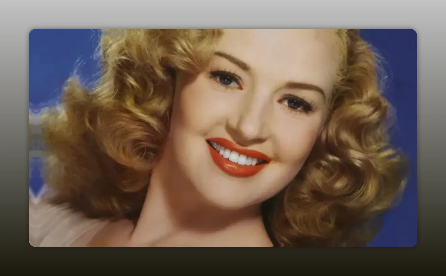 High-resolution color headshot of Betty Grable smiling with curled blonde hair and red lipstick