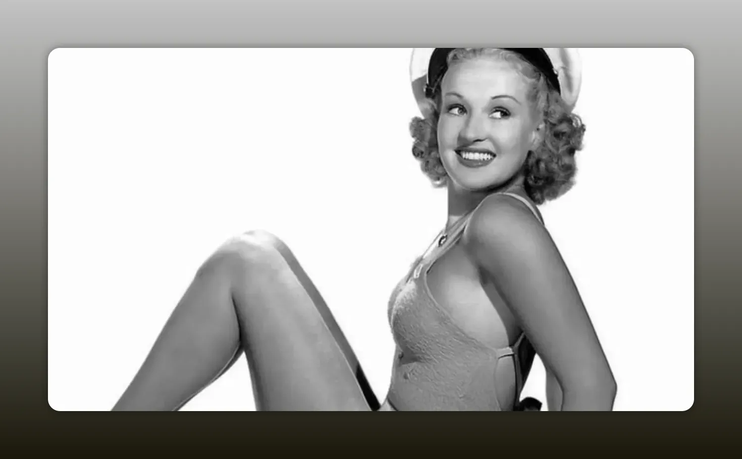 Betty Grable smiling in the famous pinup swimsuit pose with one leg bent