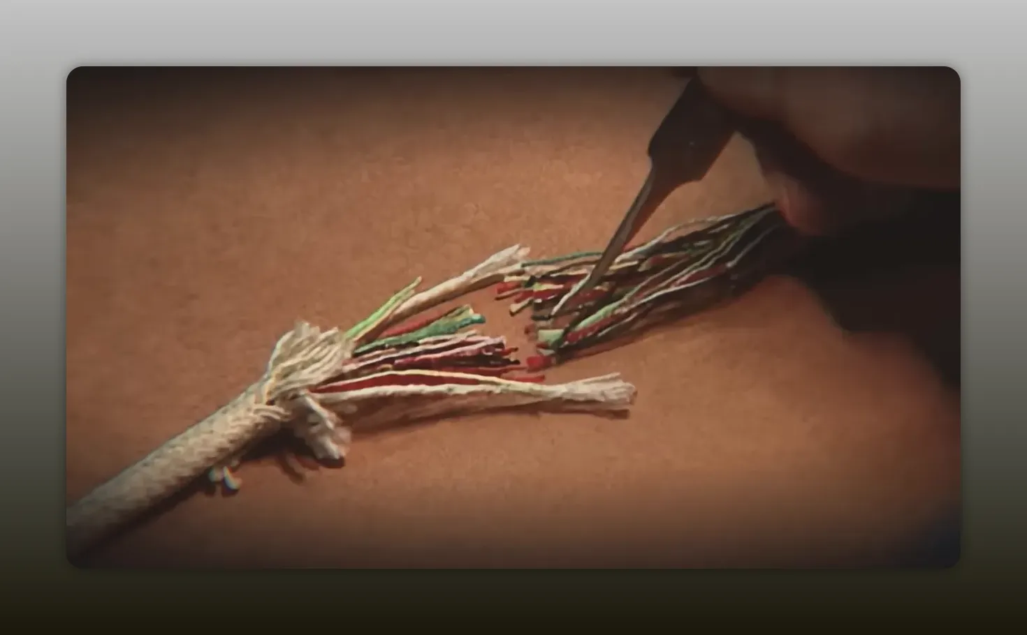 Clear close-up of frayed rope fibers being probed with a metal tool on a tabletop