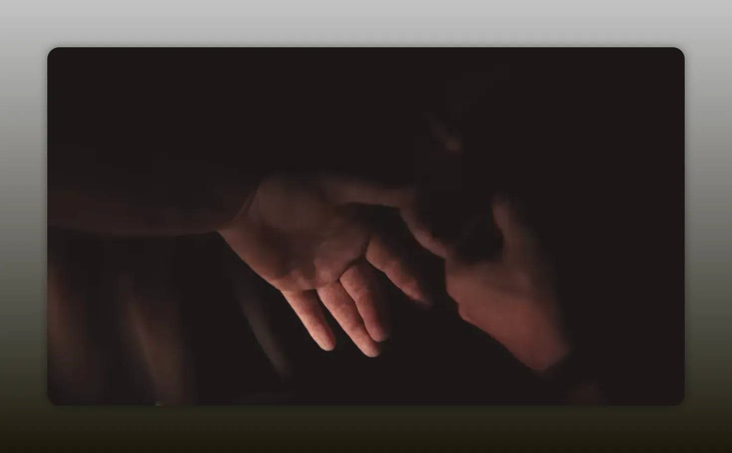 Dimly lit close-up of two hands reaching toward each other, dramatic shadows
