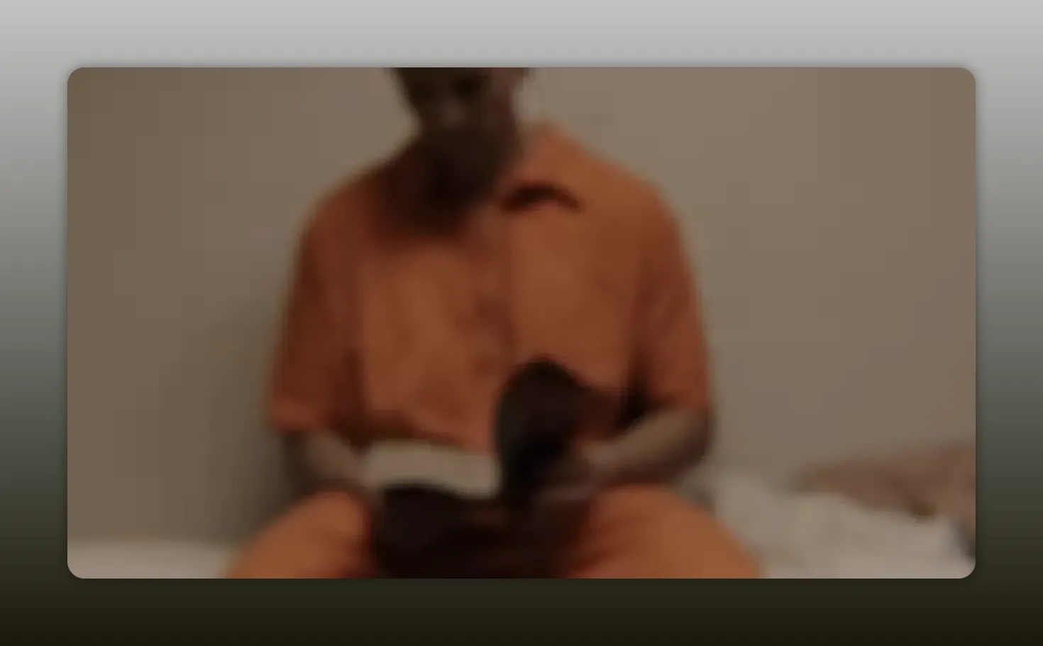 Soft-focus image of a person in an orange prison uniform seated and looking down