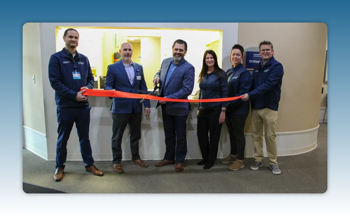 Full clinic team standing together holding a red ribbon as scissors are used to cut it at the new orthopedic clinic entrance