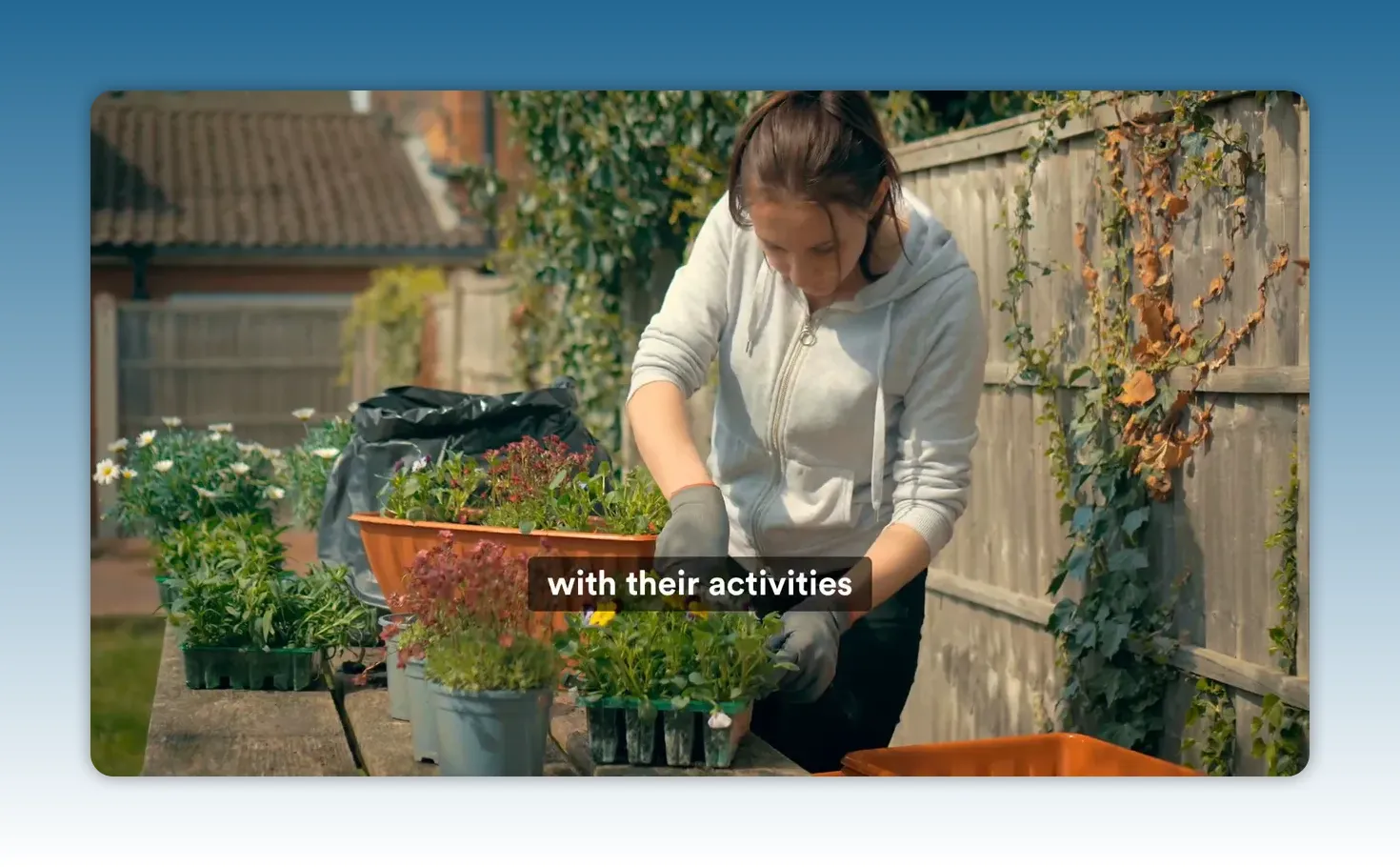 Person gardening at a table planting flowers, wearing gloves beside a wooden fence