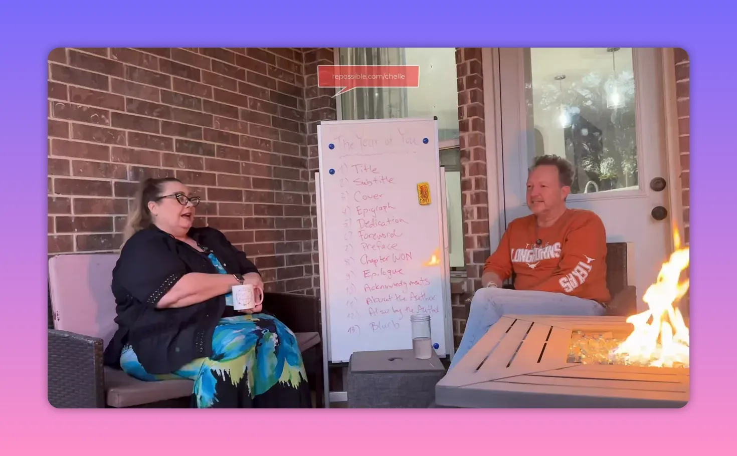 Clear shot of two people seated on a patio with a legible whiteboard titled 'The Year of You' listing sections; a firepit is visible at right.