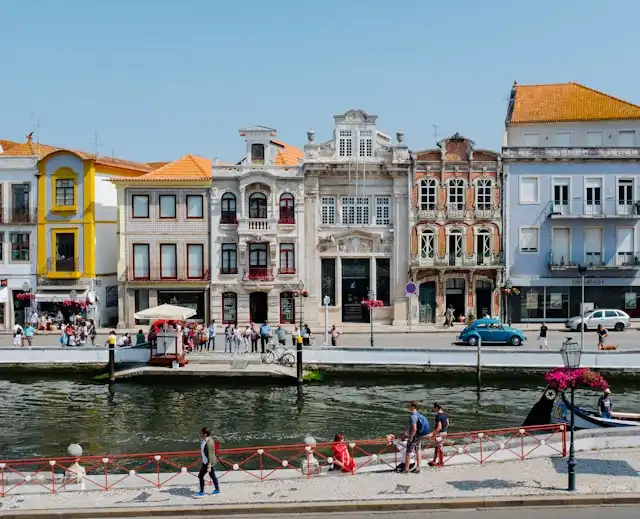 Colorful historic buildings along a canal in Aveiro, Portugal with people walking and sitting by the water.