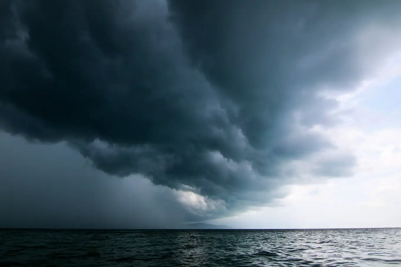 A dark storm cloud over a calm sea in Thailand, signaling an approaching storm.