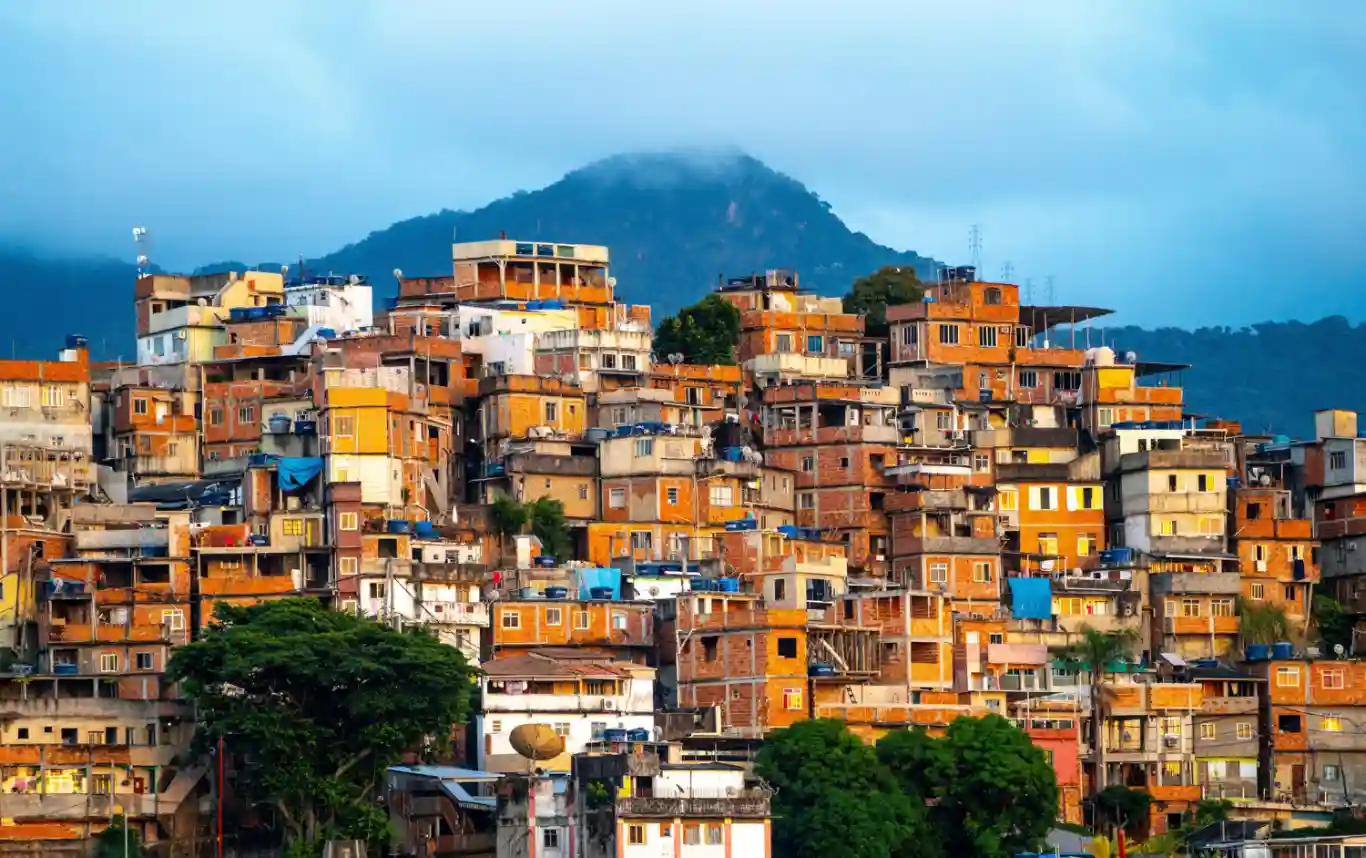 Favela in Rio de Janeiro with densely packed housing on a hillside under a cloudy sky.