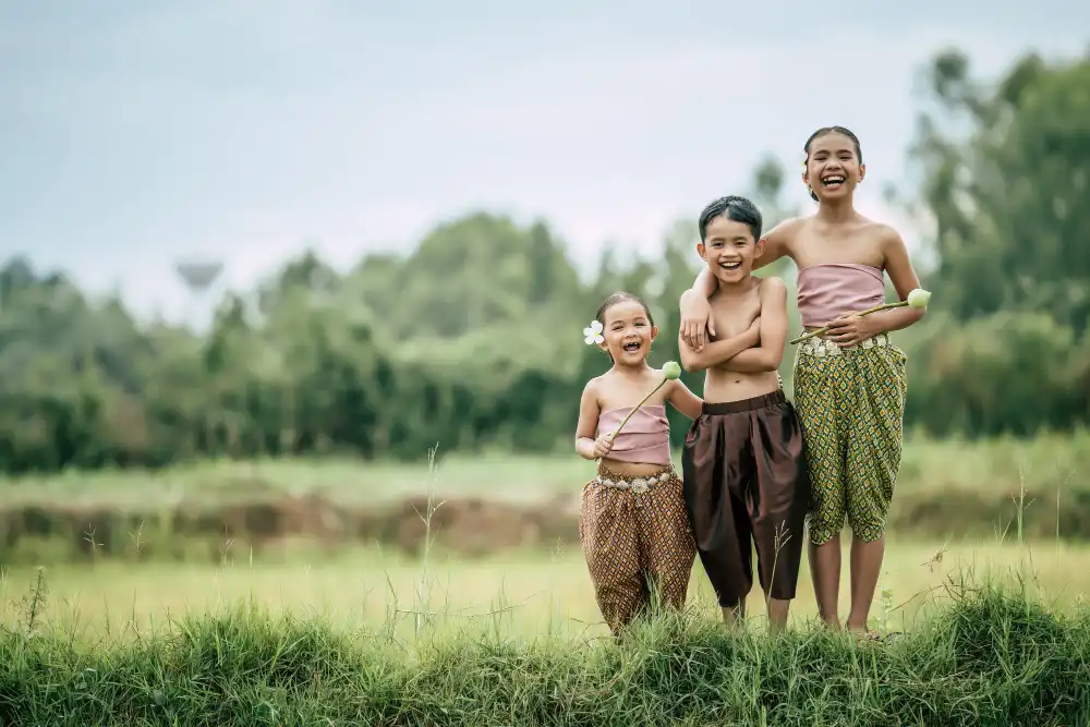 Portrait of boy and two girls in Thai traditional dress put beautiful flower on her ear standing in rice field, laughing