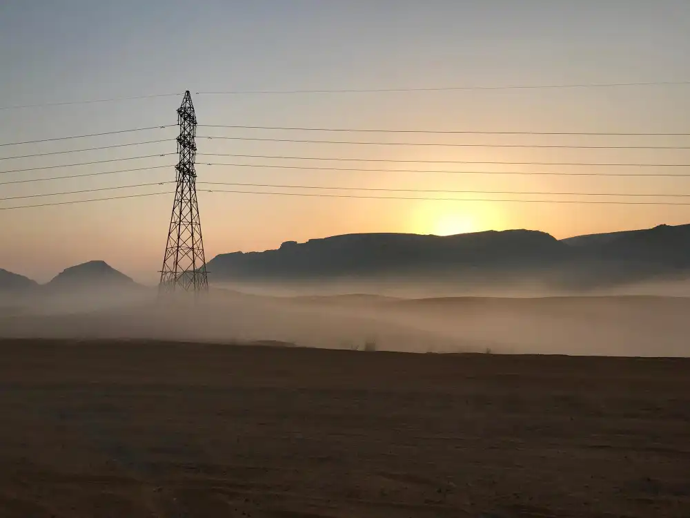  A power line tower silhouetted against a sunrise with mist over the landscape.