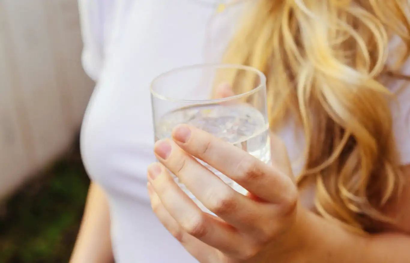 Picture of a person holding a glass of water with a focus on the glass. 