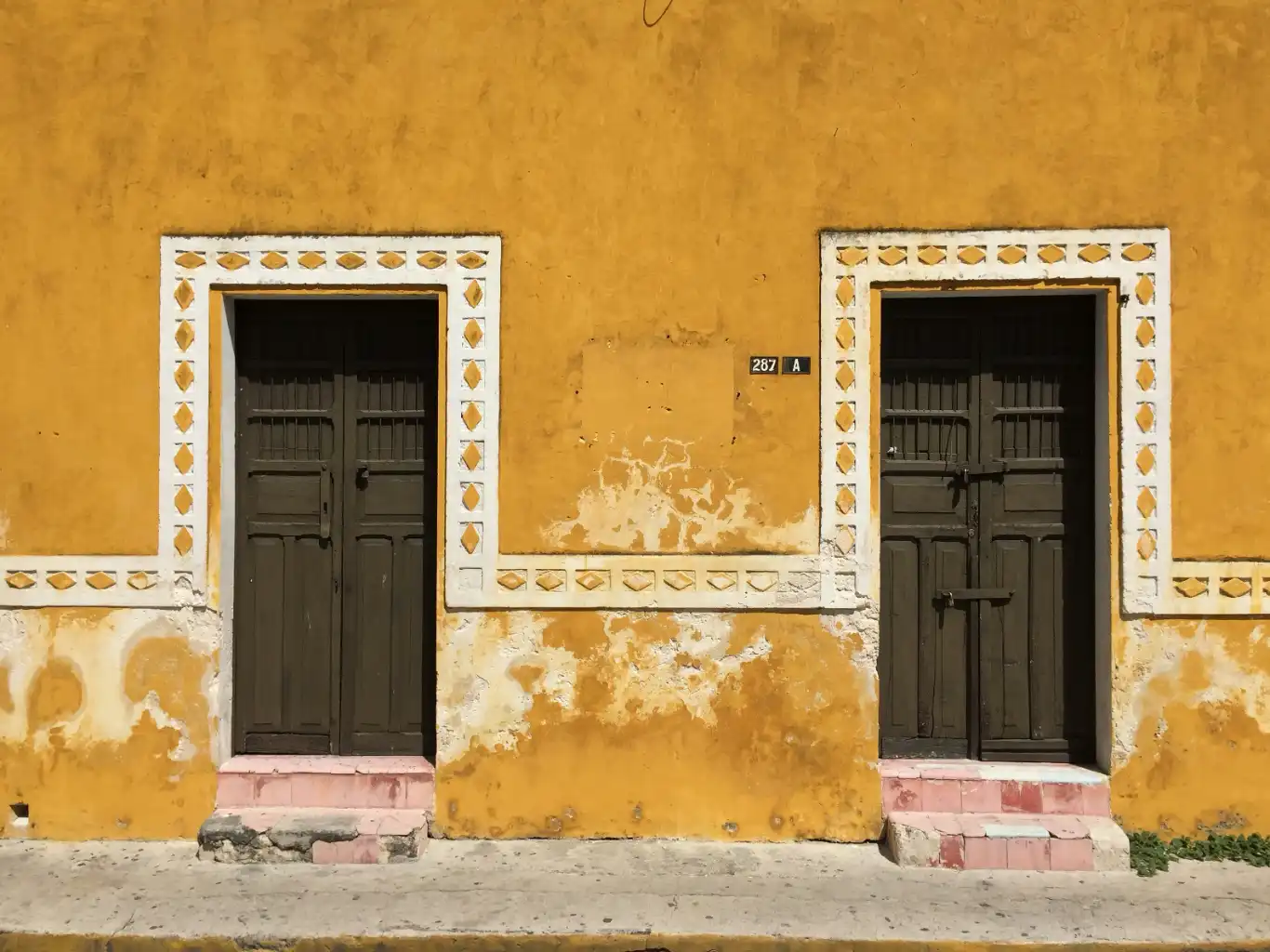 Two traditional wooden doors on a weathered mustard-yellow wall with white decorative trim.