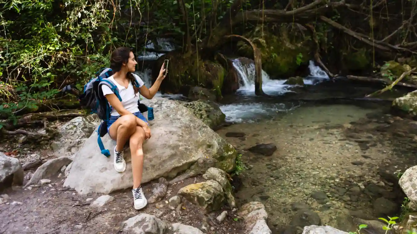 Female hiker taking a photo with her smartphone by a clear forest stream in Costa Rica.