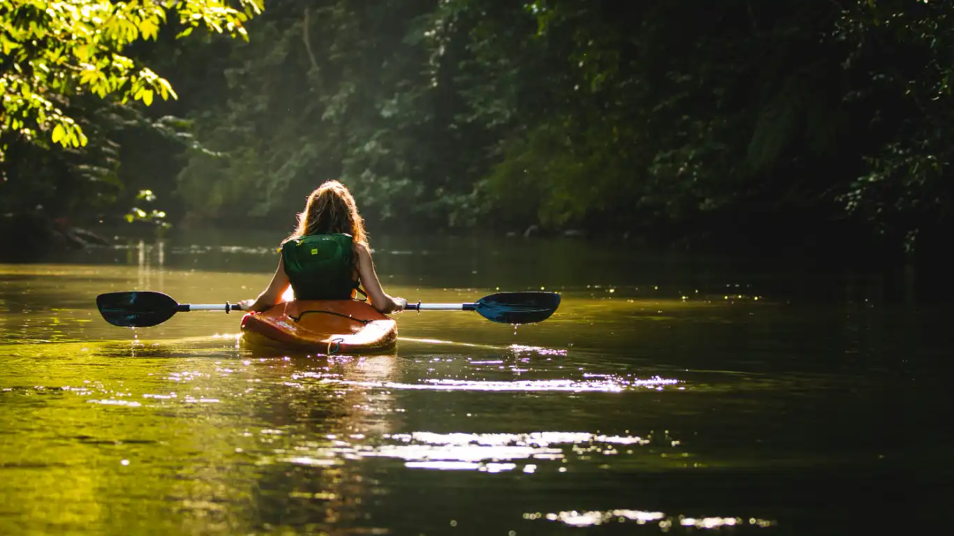 Woman kayaking in a serene, sunlit river surrounded by dense Costa Rican jungle