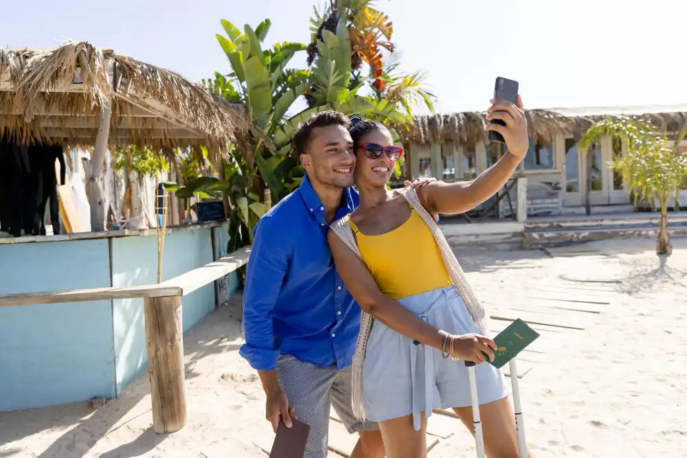 Young woman taking selfie with boyfriend over cellphone while standing at beach. 