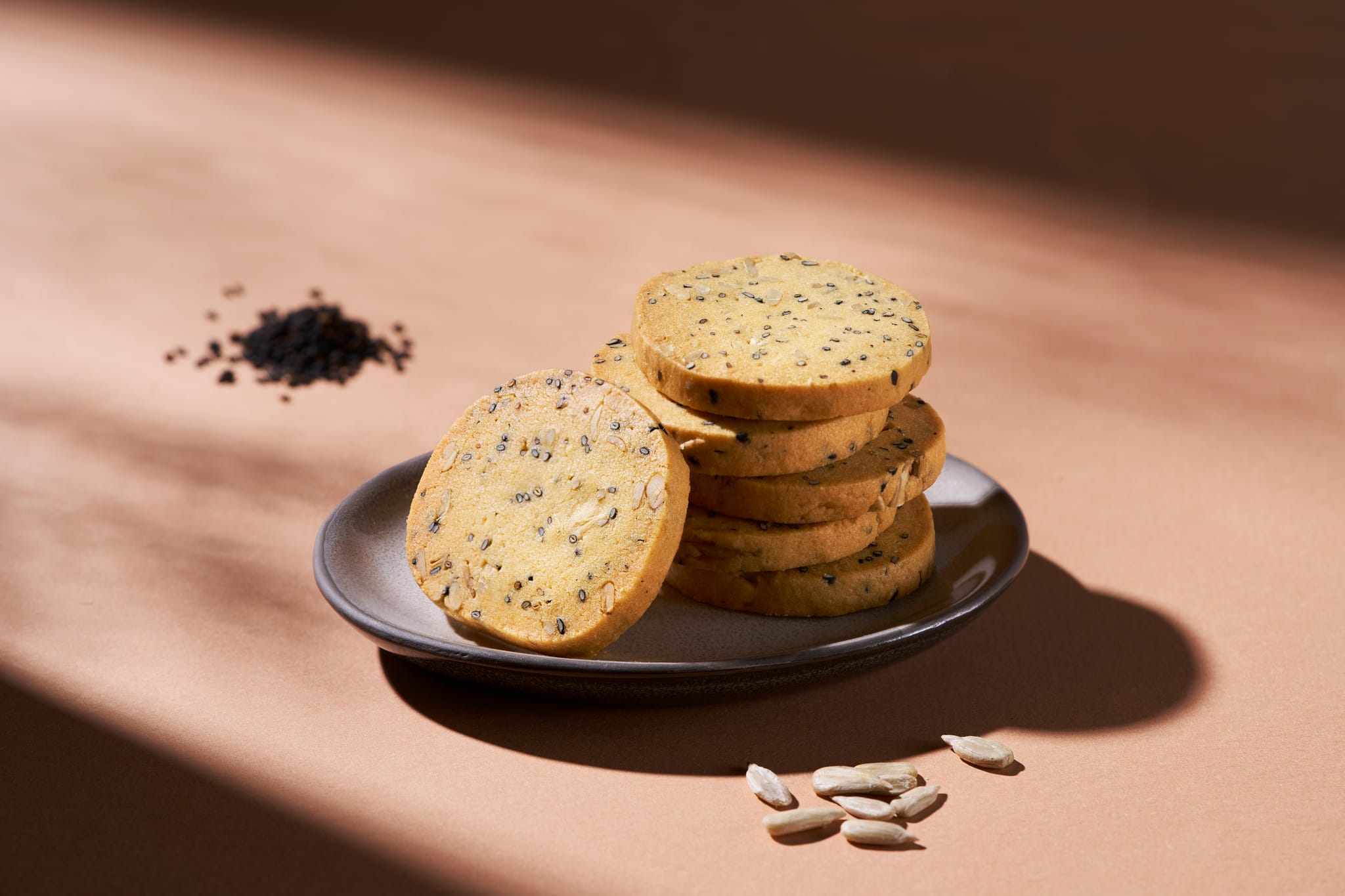 多片圓形手工餅乾堆疊,表面佈滿黑芝麻與葵花籽,呈現自然質樸的美味。