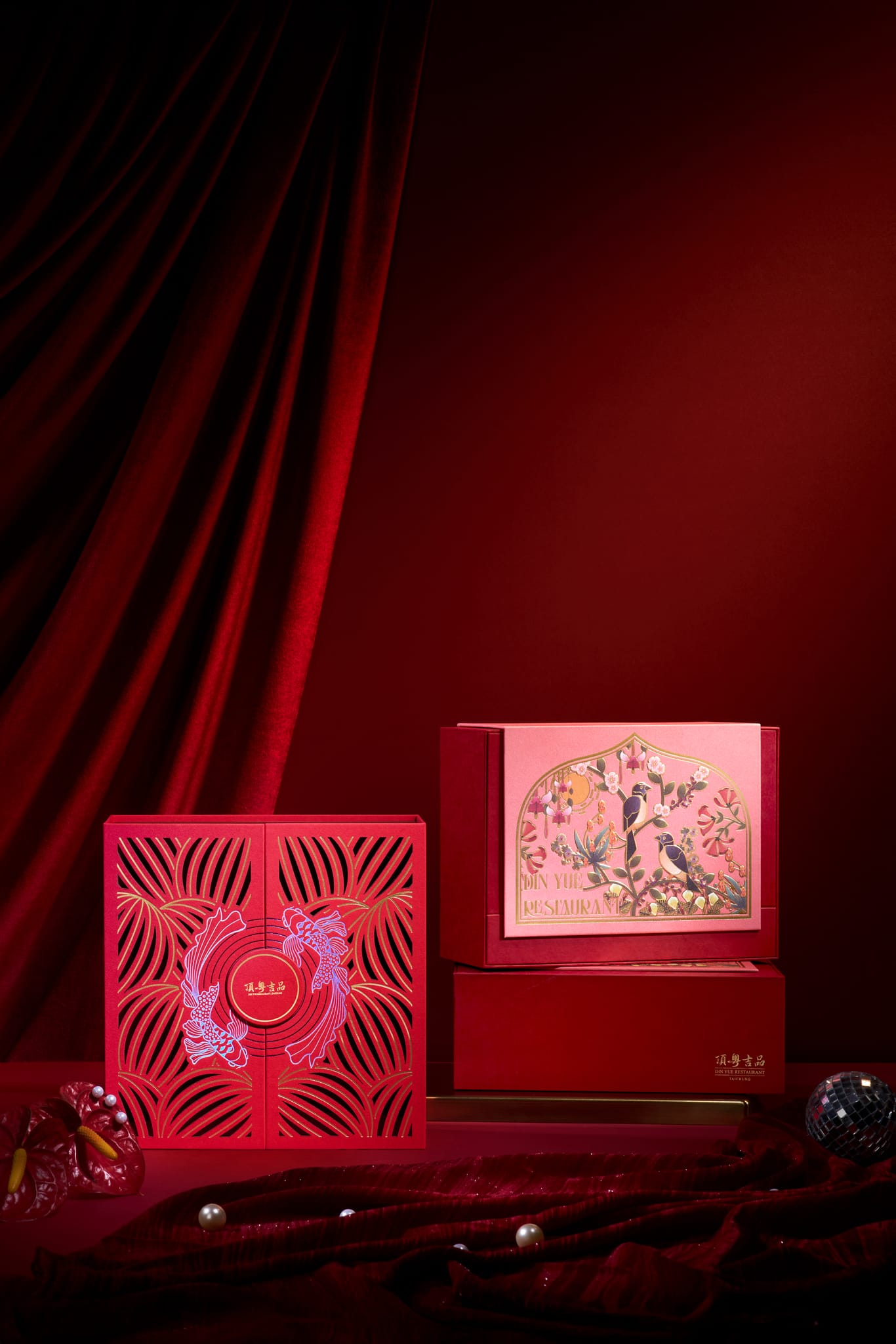 華麗紅絲絨佈景中，兩款新年禮盒：一為燈籠鏤空設計，一飾花鳥圖騰，盡顯尊貴。