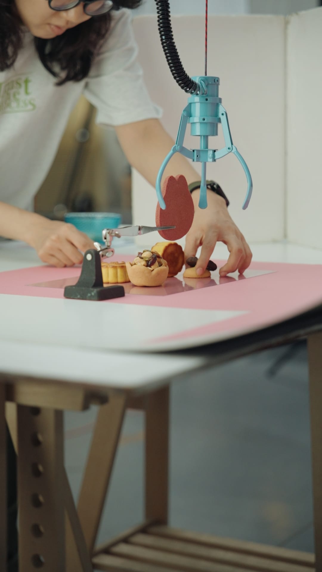 攝影師在粉色背景紙上調整聯名餅乾與道具，為拍攝做準備。