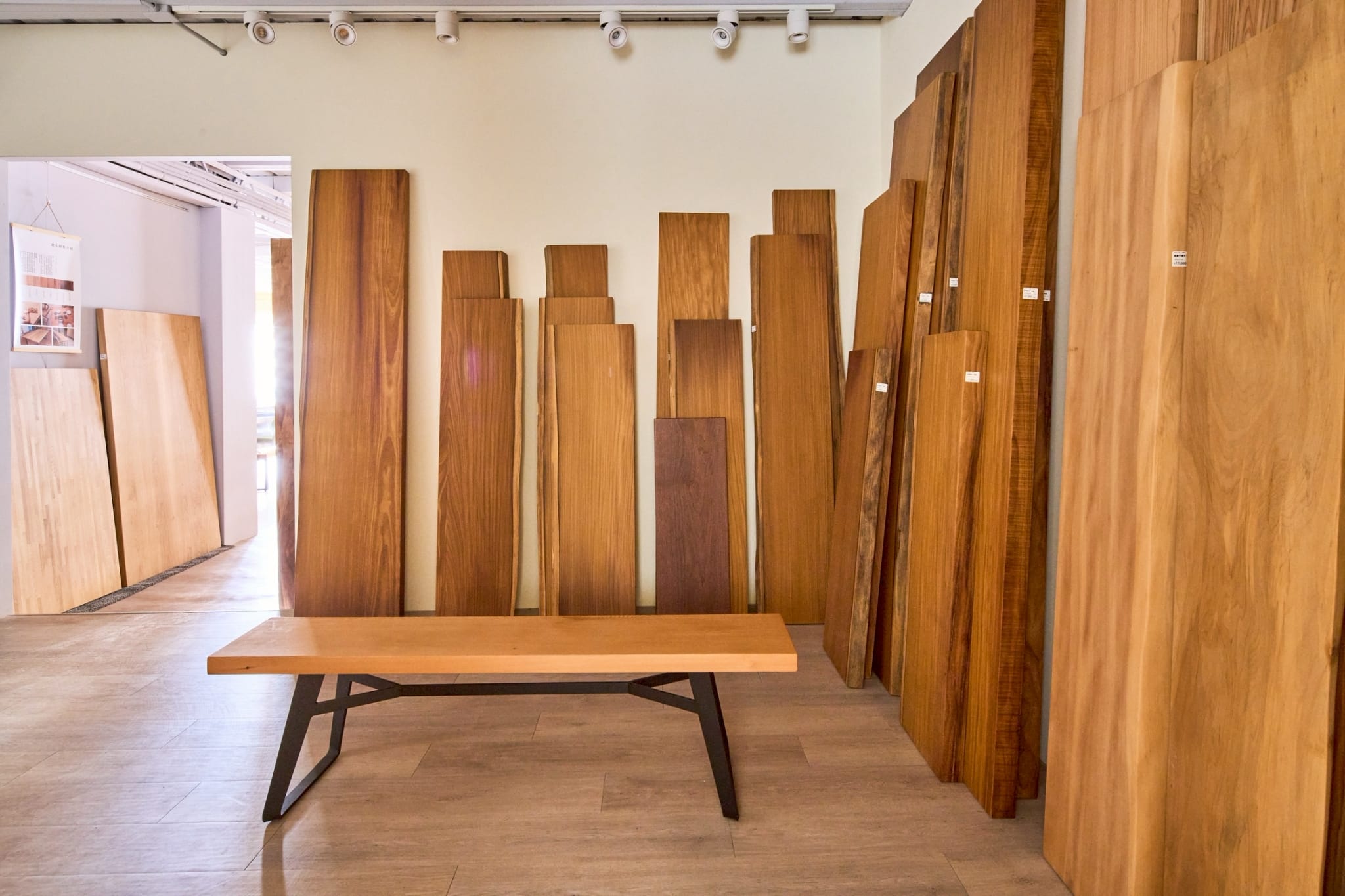 製材所空間展示多種原木板材，一張精緻木桌置於前方。
