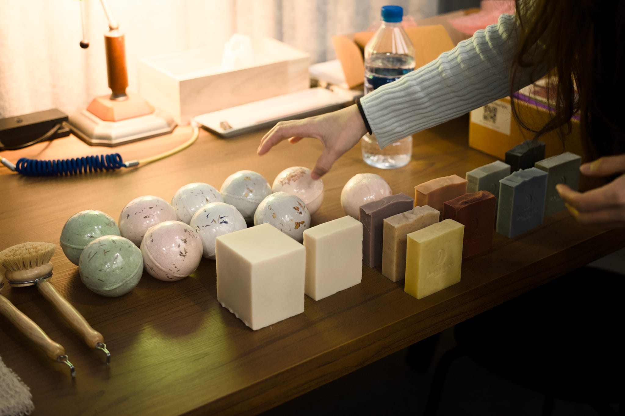 創辦人正細心陳列著多款色彩繽紛的手工皂，方形、圓形各異，呈現品牌天然純粹的美學。