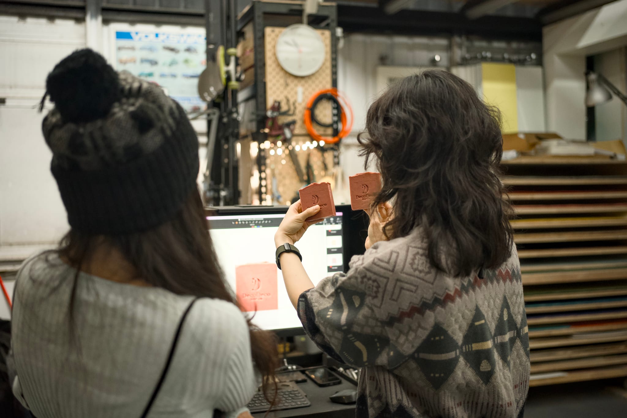 攝影師與品牌創辦人討論肥皂樣態，螢幕上顯示設計稿，手中拿著實際的肥皂樣本進行比較。