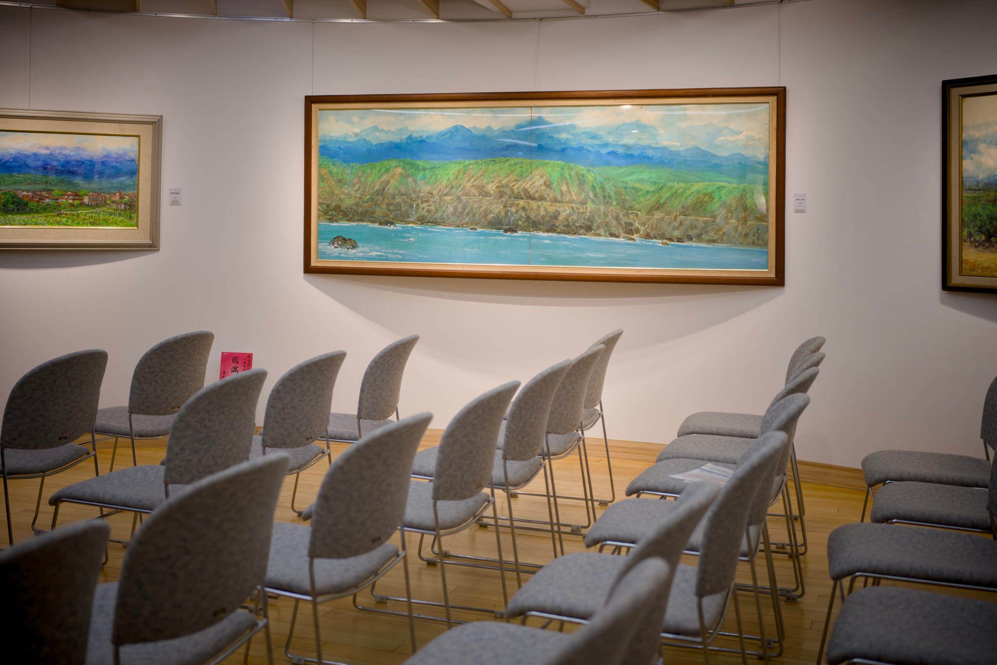 李澤藩美術館展覽會場，座位整齊排列，牆上掛著多幅畫作，其中顯眼的是《蘇花公路》，呈現大師的「一條線」美學。