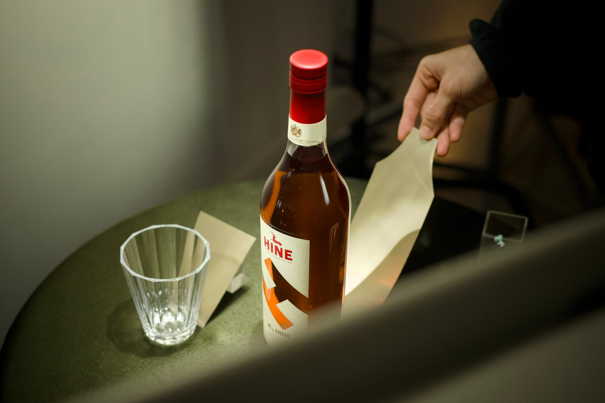 攝影師的手將金黃色反光卡隱藏在干邑酒瓶後方，為背打光技術點亮琥珀色酒液做準備。