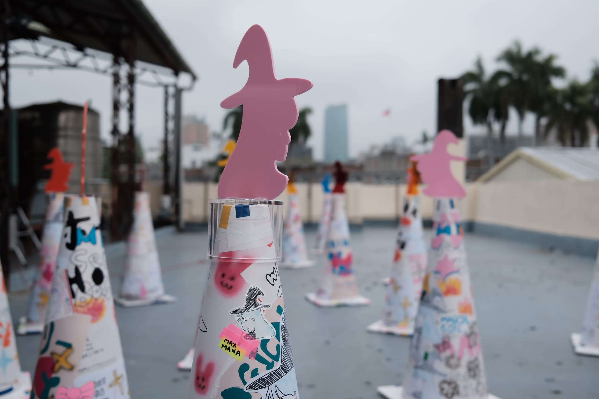 色彩鮮豔的交通錐在屋頂展示,頂部有粉色魔法少女剪影。