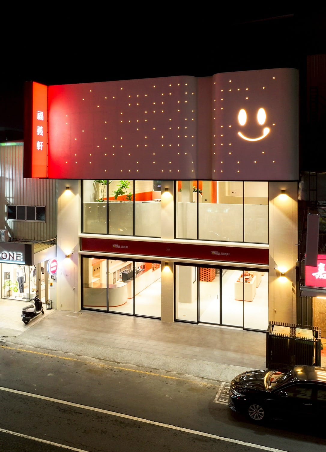 一棟夜間發光的現代門市建築，牆面以點點燈光和巨大笑臉點綴，展現年輕與設計感。
