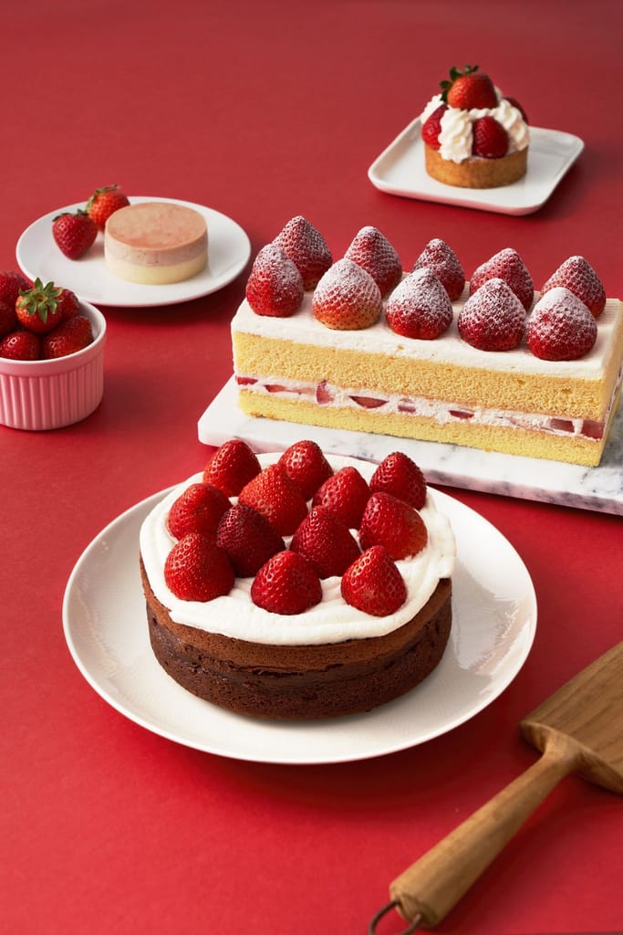 紅色背景上的多款草莓甜點，包括長條蛋糕、圓形蛋糕和塔，襯托草莓季的美味。
