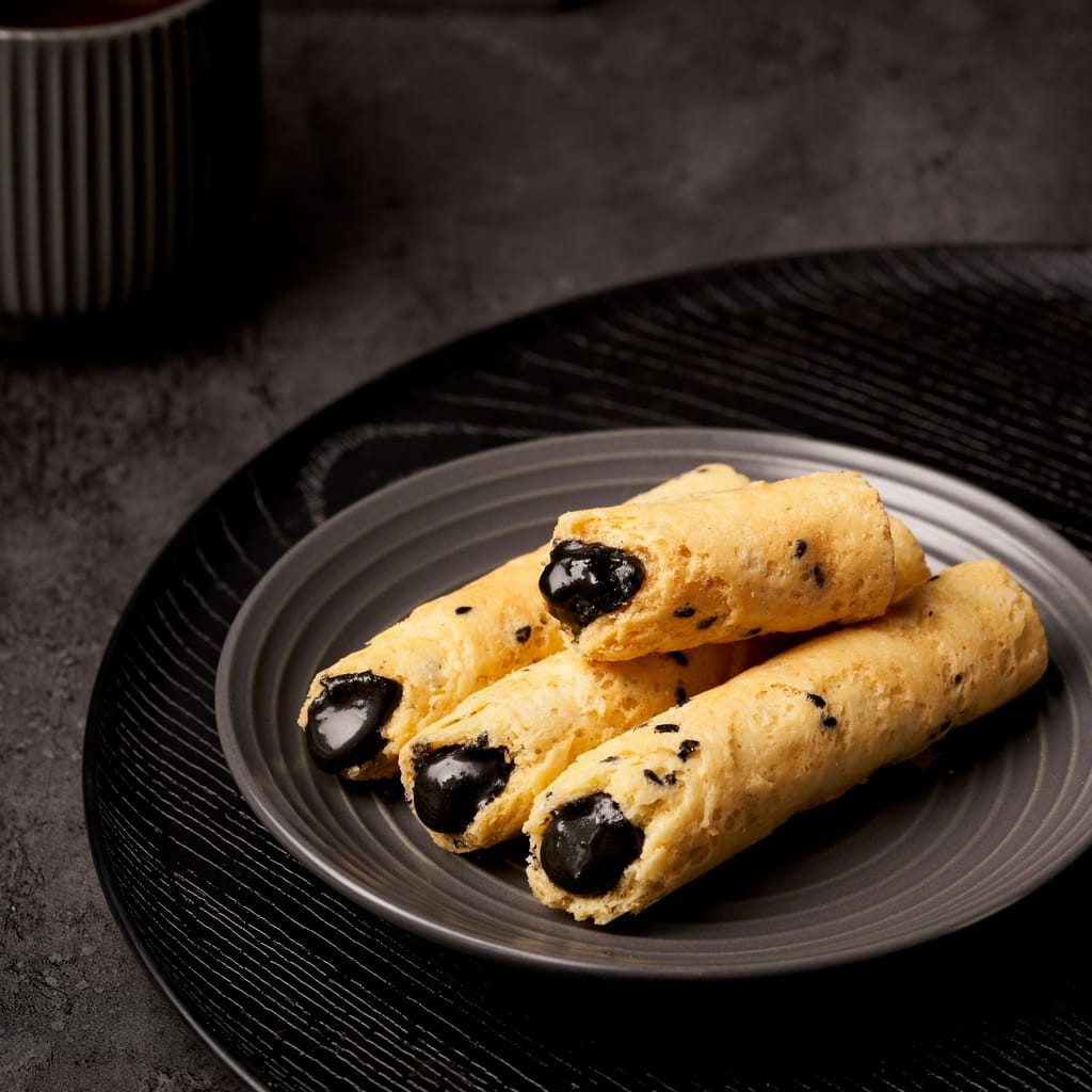金黃酥脆的蛋捲中填滿深色內餡，置於深色盤中，呈現簡約雅緻的情境。