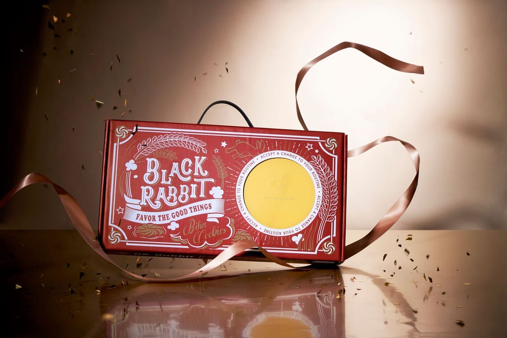 黑色小白兔新年禮盒，紅底金字設計，搭配彩帶與金粉，展現節慶氛圍。