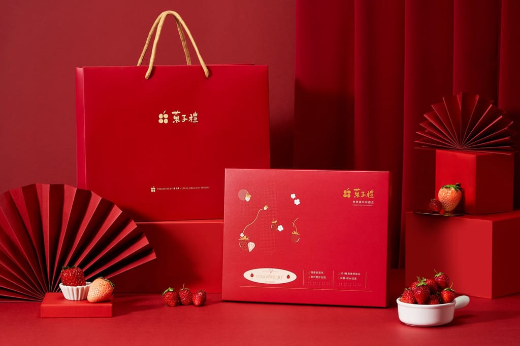 紅色背景襯托下，精美草莓禮盒與提袋，搭配新鮮草莓與中式裝飾，展現高雅節慶氛圍。