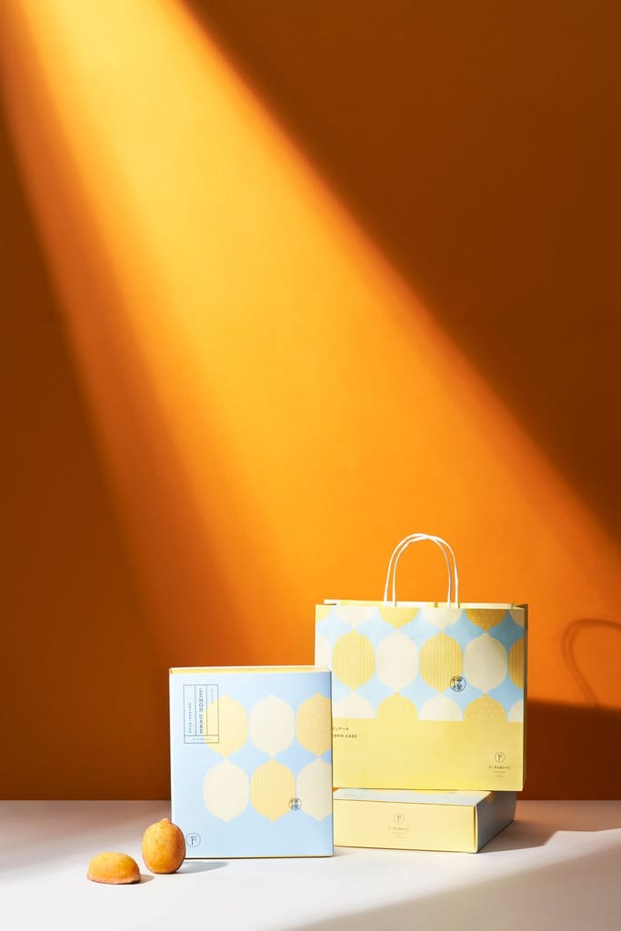 1%bakery中秋禮盒，藍黃檸檬圖案包裝與手提袋，搭配橘色背景光束。