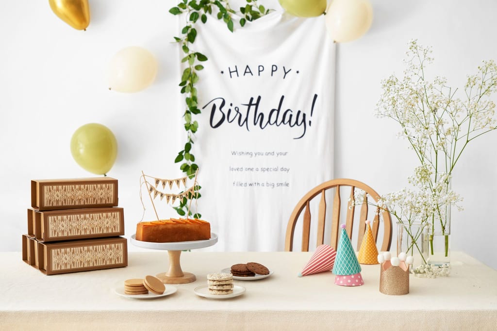 生日派對蛋糕佈置，桌上有蛋糕、禮盒、餅乾和氣球，背景有生日快樂橫幅。