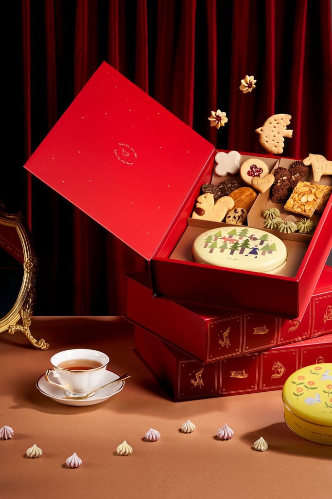 紅色童話故事書禮盒開啟，內裝多樣餅乾，配上茶杯與散落甜點。