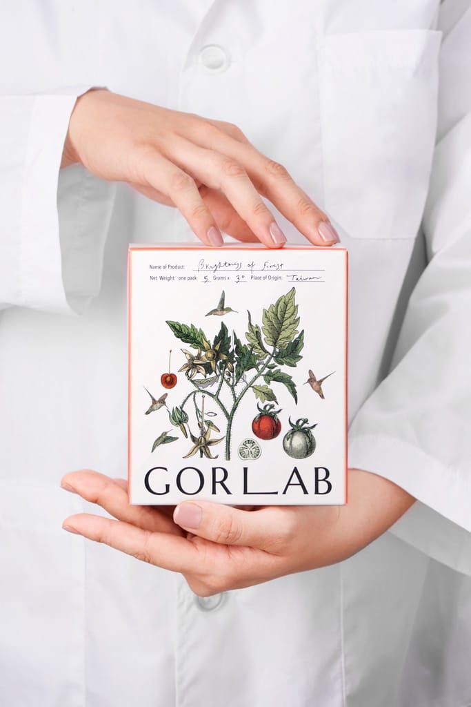 身穿白袍的手捧GORLAB森林光膠原蛋白產品，盒身飾有植物圖案。