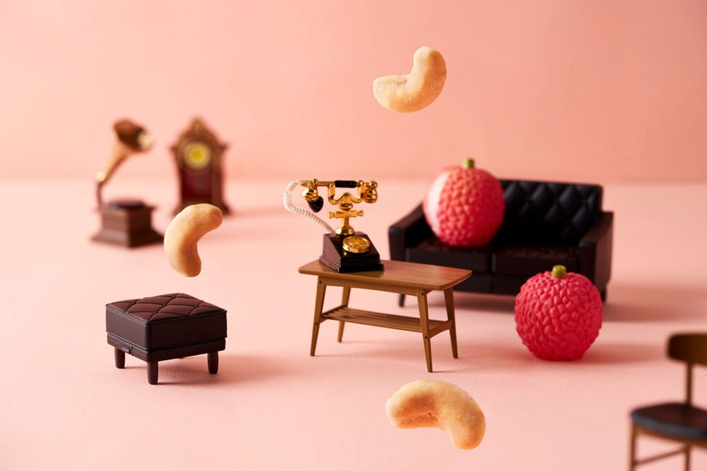 粉色背景上，腰果輕盈漂浮於迷你家具間，創意呈現「口味堅果」的獨特風味與玩趣意象。